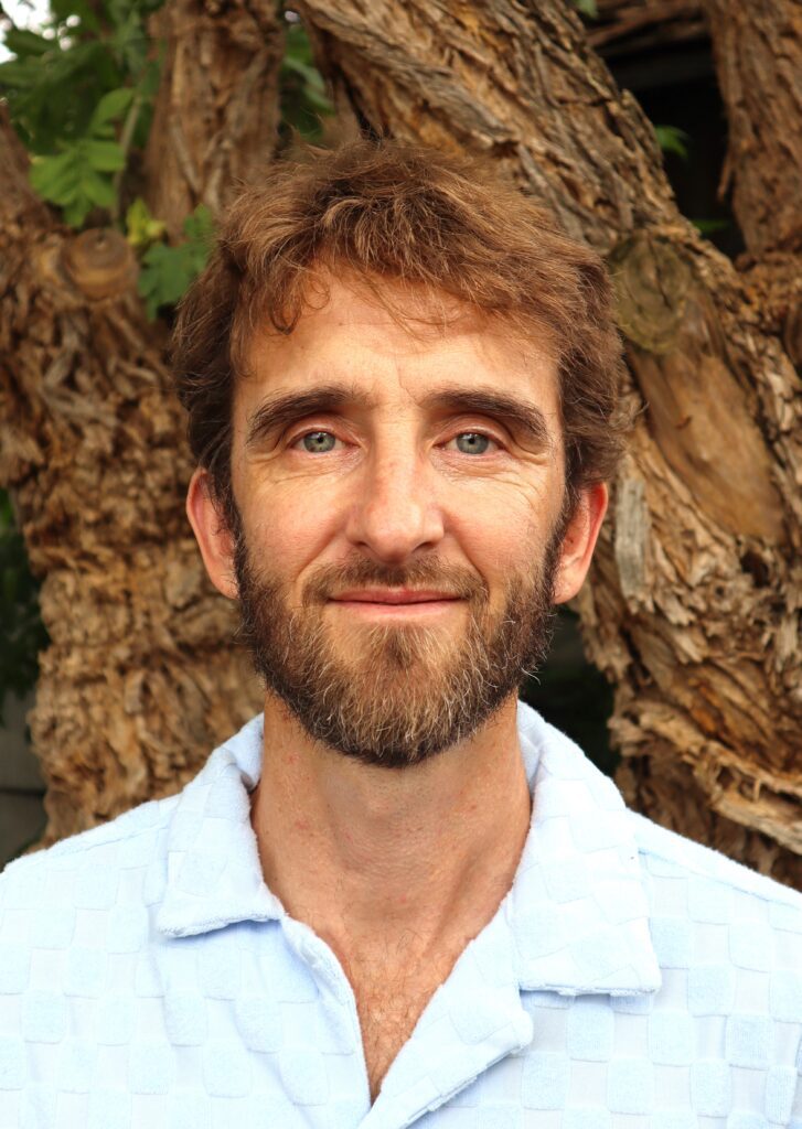 Man with beard, blue shirt, smiling.